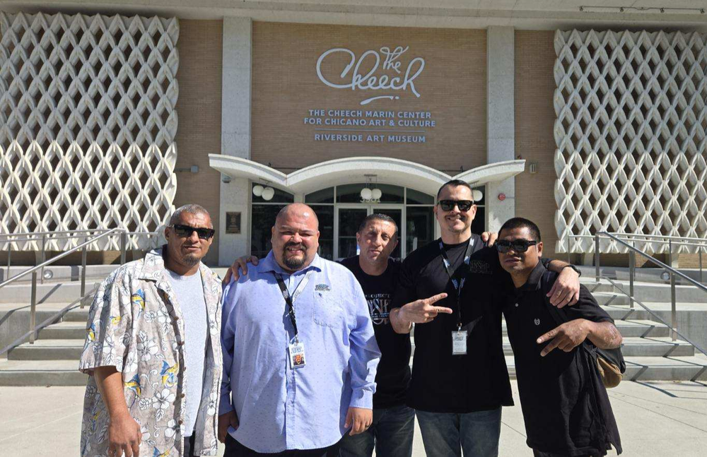 Five men smiling and posing on the steps in front of The Cheech Marin Center for Chicano Art & Culture building.