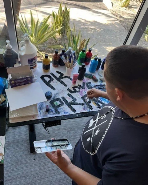 Engaging Art Session with Vibrant Paints Person painting 'PK LOVE PK' on a canvas with colorful paints and brushes, surrounded by various art supplies.