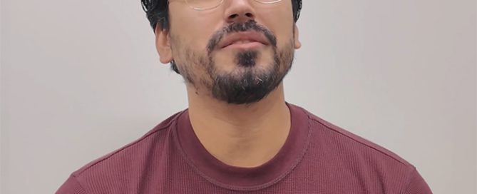 Man with beard and gold-rimmed glasses looking up, wearing a maroon waffle-knit shirt with a 'PROJECT KINSHIP' pin.
