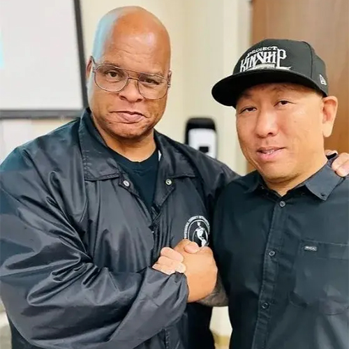 Partnership and Community Spirit: Two Men Shaking Hands Two men, one Black and one Asian, shaking hands and smiling. The Black man wears glasses and a black jacket; the Asian man w…