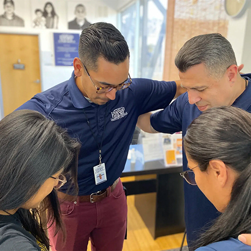 Our Team: Shared Focus and Connection Four team members, two men and two women in navy polos, huddle closely, looking down in shared focus and connection.