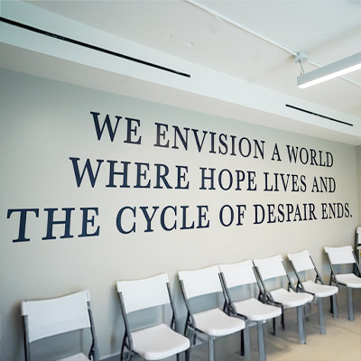 Motivational wall text 'WE ENVISION A WORLD WHERE HOPE LIVES AND THE CYCLE OF DESPAIR ENDS' in a room with white chairs.